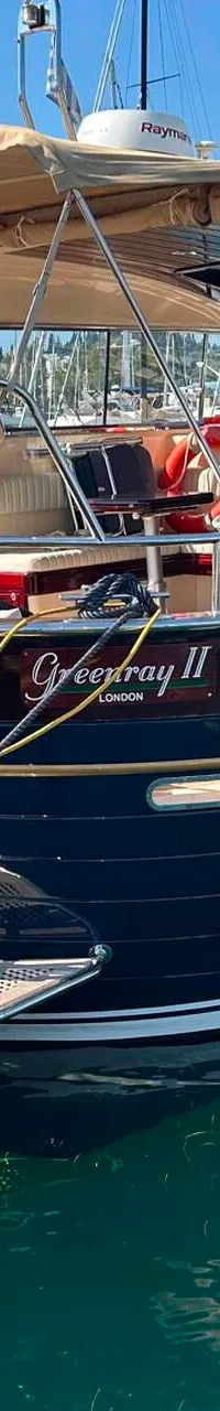 Een donkerblauwe motorboot met een beige zonnescherm en een bijbootje ligt aangemeerd in een haven. — Apreamare 12 Cabinato