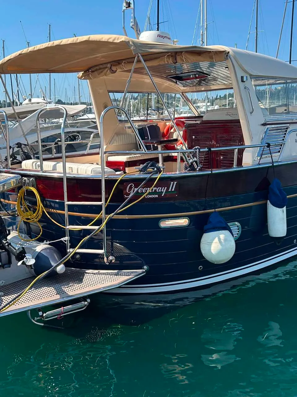 Een donkerblauwe motorboot met een beige zonnescherm en een bijbootje ligt aangemeerd in een haven. — Apreamare 12 Cabinato