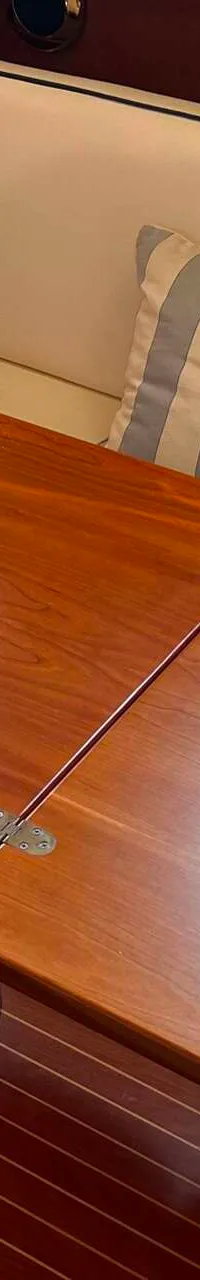 Een houten tafel met uitklapbare bladen staat in een bootkajuit met een bank en gestreepte kussens.