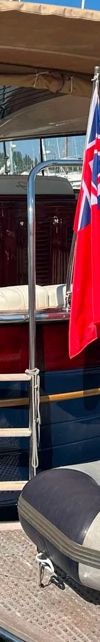 Een donkerblauwe boot met een rood-bruine opbouw en een beige zonnedek ligt in een haven met een bijboot op het zwemplateau.