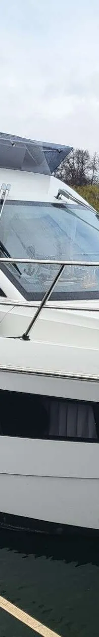 Een witte motorboot met een donkerblauwe kap en ramen, afgemeerd aan een steiger met een waterig landschap op de achtergrond.