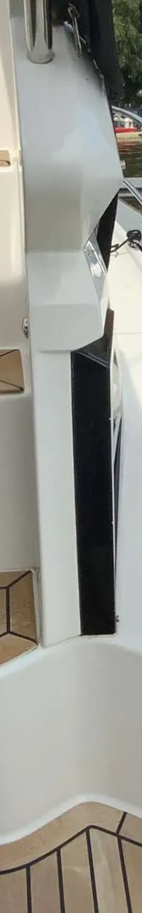 Een witte boot met teakhouten treden en een reling, afgemeerd aan een steiger met een andere boot ernaast. — Galeon 300 Fly