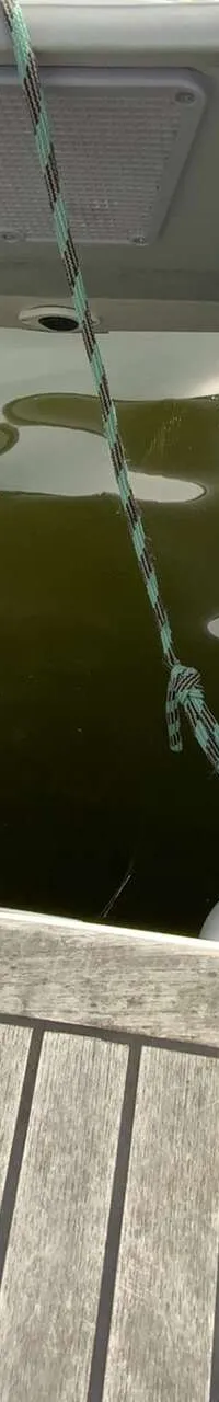 Een houten dek met twee opblaasbare bijboten die aan een davit hangen boven groen water.