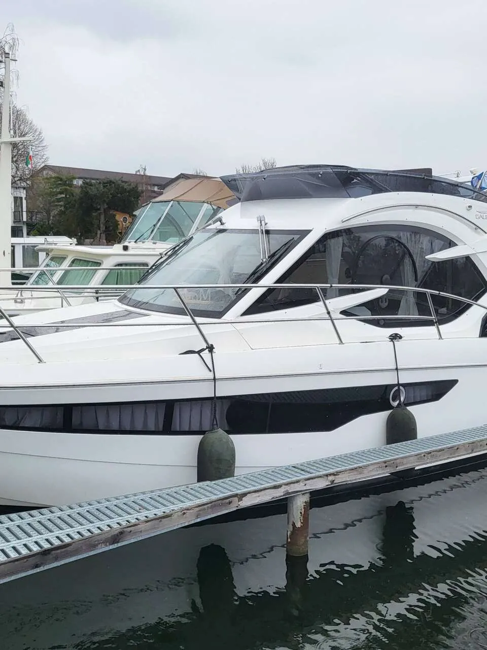 Een witte motorboot met zwarte ramen en een zwarte kap ligt aangemeerd aan een steiger. — Galeon 300 Fly