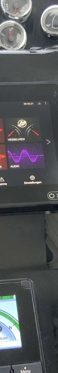 De foto toont een deel van een dashboard met diverse meters, een groot digitaal scherm, een joystick en schakelaars.