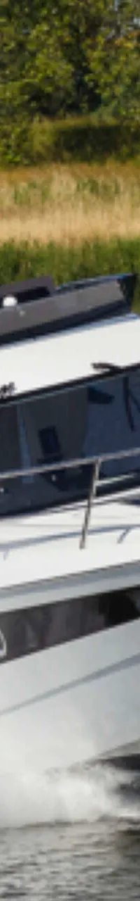 Een witte motorboot met een man aan het roer vaart over water, met een groene oever op de achtergrond. — Galeon 300 Fly