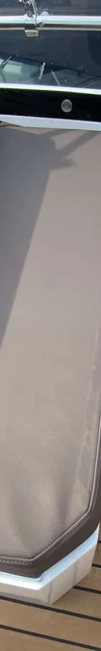 Een bootinterieur met een stuurwiel, een bank met grijze kussens en een houten dek.