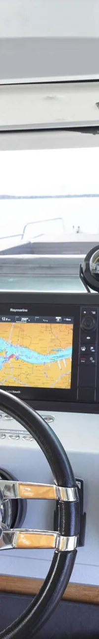 De foto toont een stuurstand met twee Raymarine navigatieschermen, een stuurwiel, gashendels en diverse bedieningspanelen.