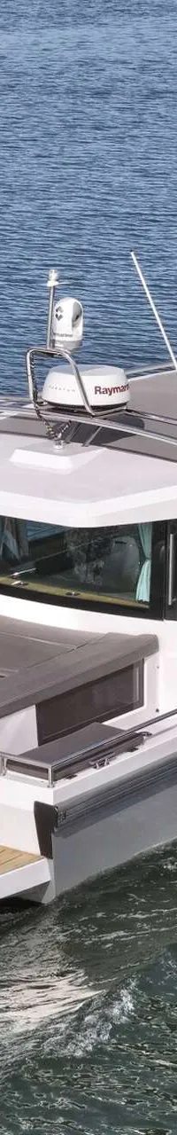 Een grijze motorboot met witte opbouw vaart op een waterweg, met een groene oever en blauwe lucht op de achtergrond.