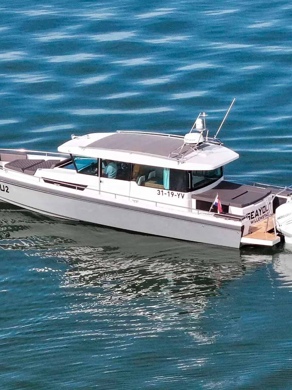 Een witte motorboot met hardtop en twee Mercury 300 buitenboordmotoren ligt in het water, met de naam 'SEAYOU2'.