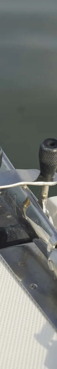 Een roestvrijstalen ankerrol met een anker en ketting is zichtbaar op de boeg van een witte boot met antislipdek.