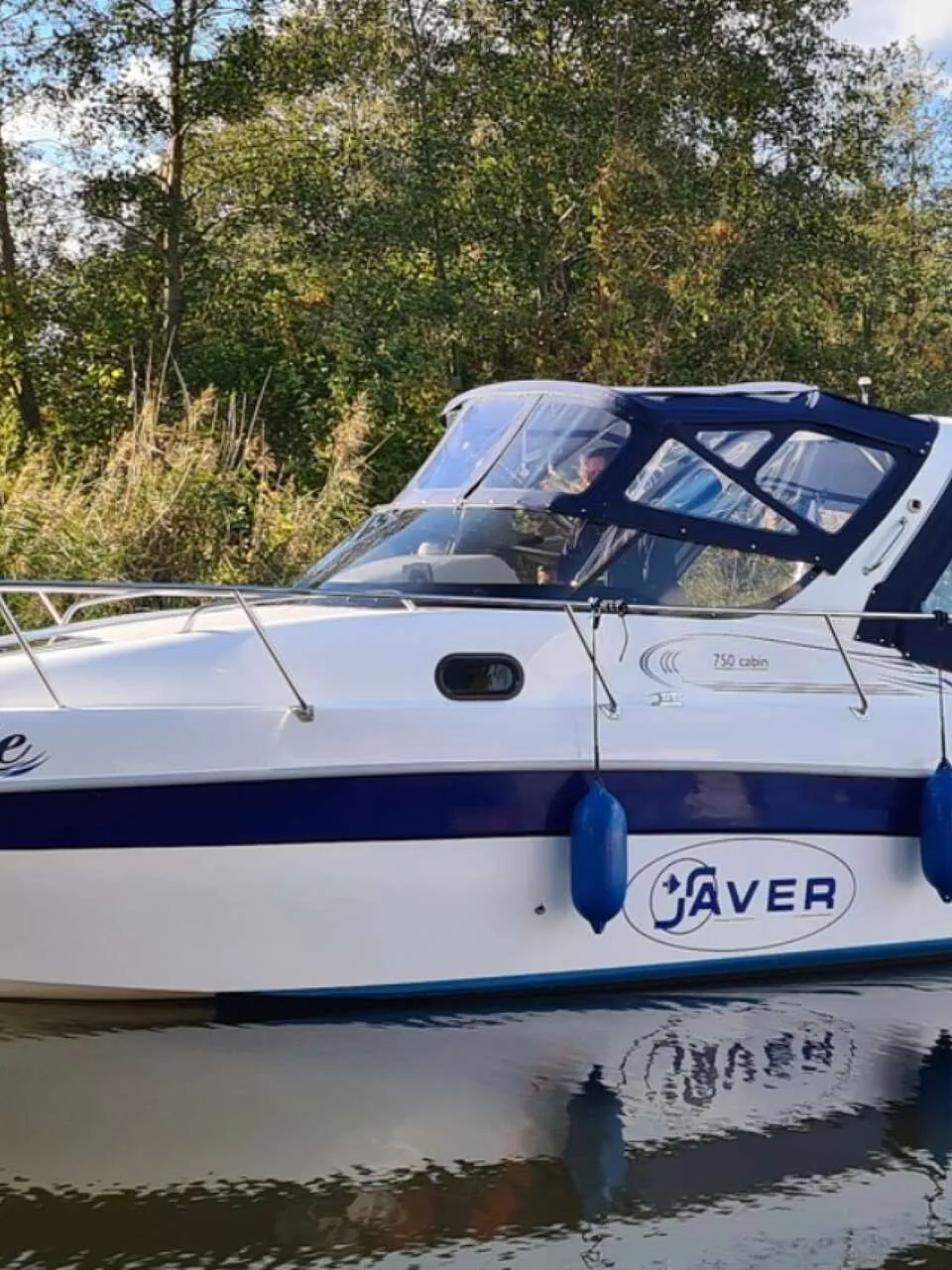 Een witte motorboot met blauwe accenten en de naam "Josie" op de boeg, drijvend op water met bomen op de achtergrond.