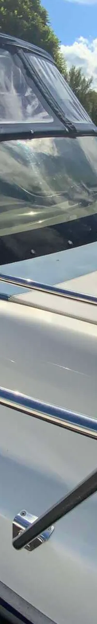 Een witte boot met een blauwe kap en een voorruit ligt aangemeerd aan een houten steiger. — Saver 750 Cabin
