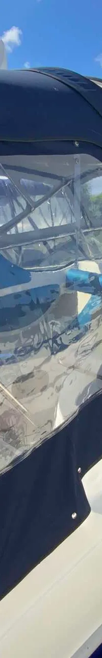 Een witte boot met blauwe strepen en een blauwe kap ligt aangemeerd aan een houten steiger, met blauwe stootwillen.