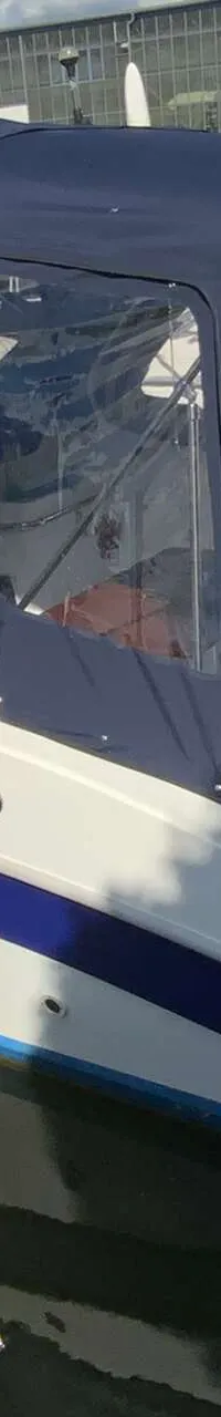 Een witte boot met blauwe strepen en een blauwe kap ligt in het water, met een Suzuki buitenboordmotor zichtbaar.