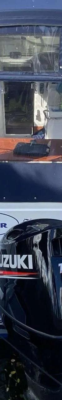 Een witte boot met een blauwe kap en een Suzuki 150 buitenboordmotor ligt in het water, omringd door andere boten.