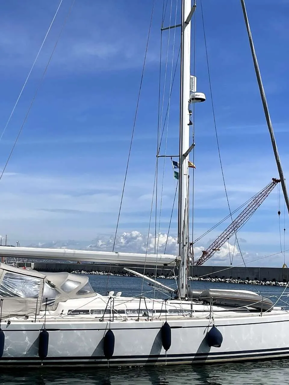 Een witte zeilboot met een grijze buiskap en stootwillen ligt in het water onder een blauwe lucht. — Arcona 430