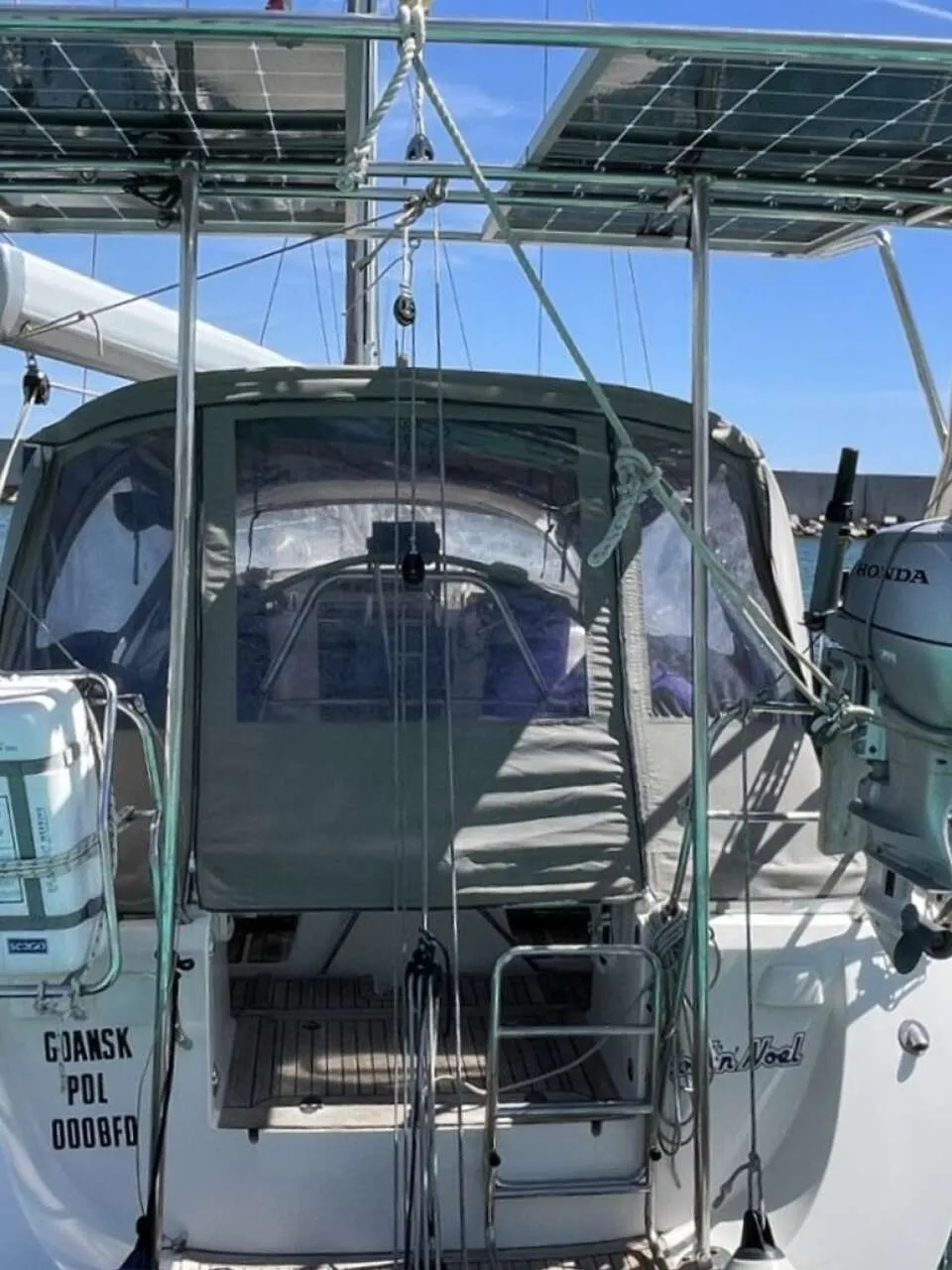 De achterkant van een witte zeilboot met een grijze buiskap, een Honda buitenboordmotor en zonnepanelen. — Arcona 430