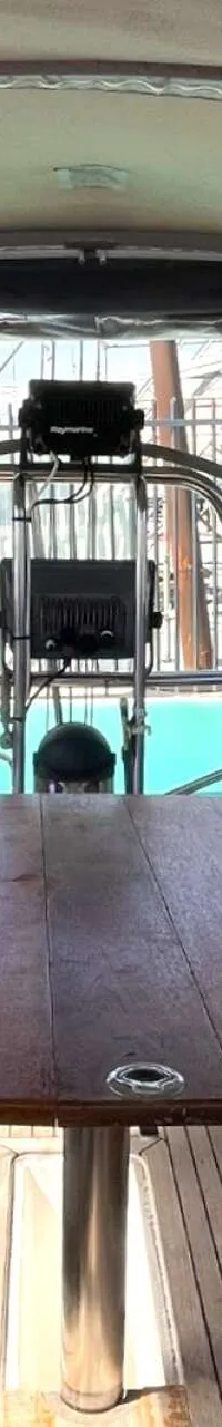 De foto toont de kuip van een zeilboot met een houten tafel, paarse kussens en een stuurwiel met navigatie-instrumenten.