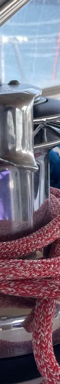 Een zilverkleurige lier met rode en blauwe lijnen op een wit dek, met een raam en een logo van "DE VALK YACHT BROKERS" op…