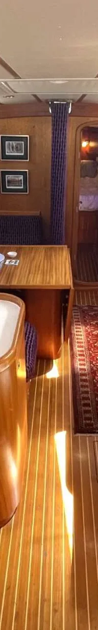 De foto toont het interieur van een boot met een houten vloer, een kombuis, zitbanken en een tafel. — Arcona 430