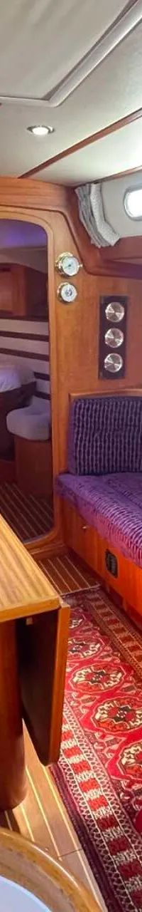 De foto toont het interieur van een boot met houten wanden, paarse banken, een houten tafel en een rood tapijt. — Arcona 430