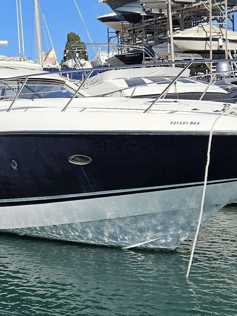 Een witte en donkerblauwe motorboot ligt in het water, met stootwillen aan de zijkant en een touw aan de boeg.
