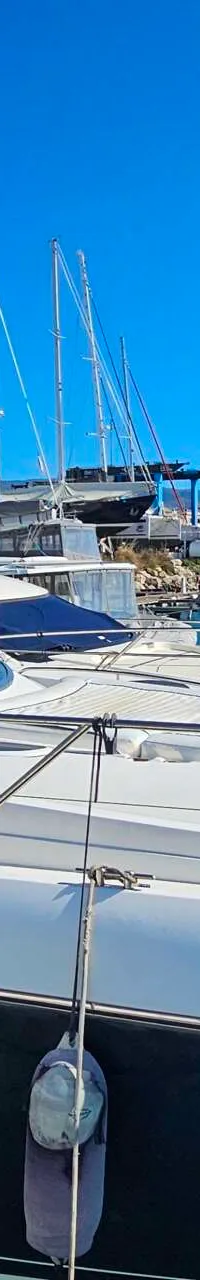 Een witte motorboot met donkerblauwe romp ligt in een jachthaven, omringd door andere boten en zeilboten.