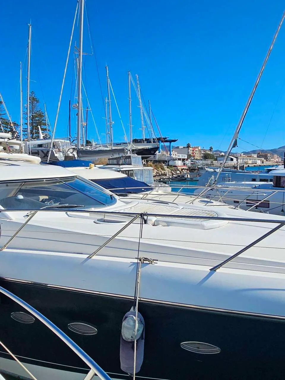 Een witte motorboot met donkerblauwe romp ligt in een jachthaven, omringd door andere boten en zeilboten.