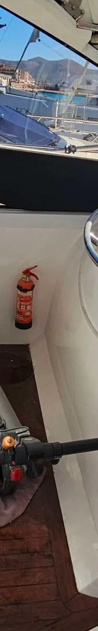 De foto toont een interieur van een boot met witte banken, een houten vloer, een brandblusser en een elektrische step.