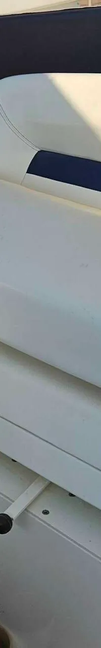 Een witte bootstoel met blauwe accenten en zwarte biezen, met een houten stuurwiel en een stofzuiger op de voorgrond.