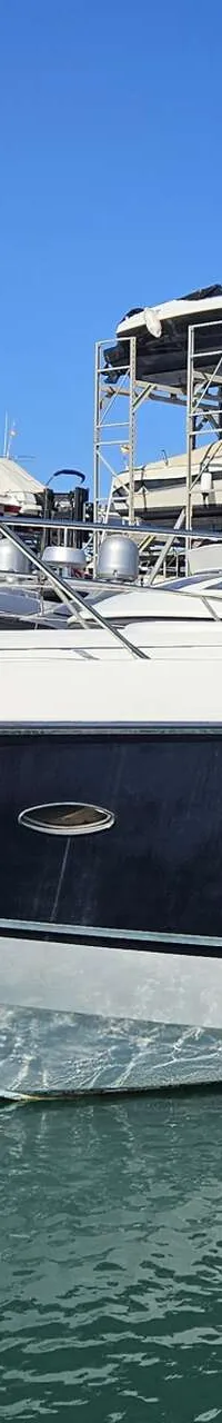 Een witte en donkerblauwe motorboot ligt afgemeerd in een haven, met andere boten op de achtergrond. — Sunseeker Portofino 53