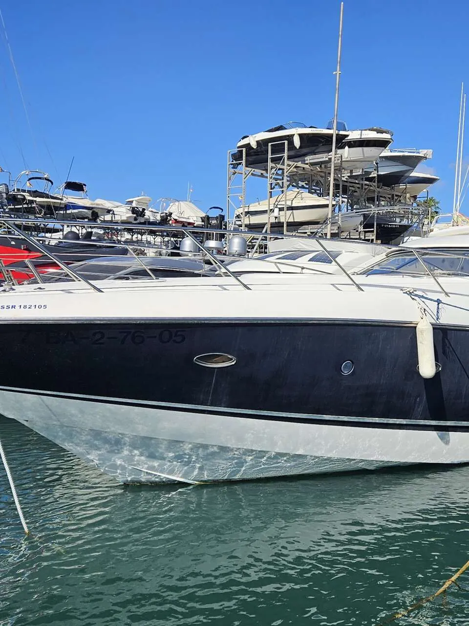 Een witte en donkerblauwe motorboot ligt afgemeerd in een haven, met andere boten op de achtergrond. — Sunseeker Portofino 53