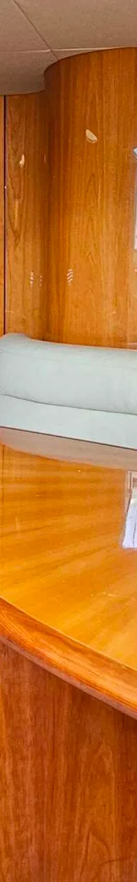 Een interieur van een boot met een houten tafel, een beige bank met kussens, een keukenblok en een deur.