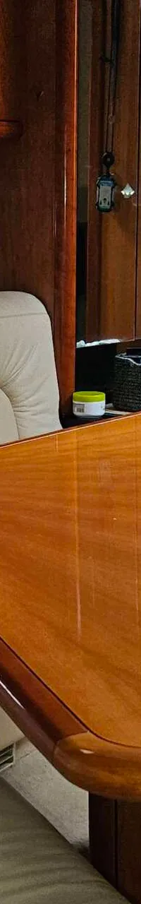 Een interieur van een boot met een beige bank, oranje en donkerblauwe kussens, een houten tafel en een trap.