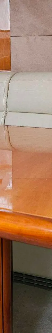 Een glanzende houten tafel met een crèmekleurige bank met oranje en donkerblauwe kussens.
