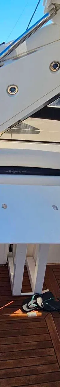 Een bootdek met witte banken, een witte tafel, een houten vloer en twee kussens.