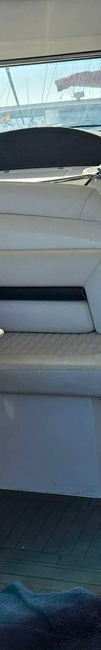 Een bootinterieur met een witte bank, een tafel, oranje en blauwe kussens, en een houten vloer.