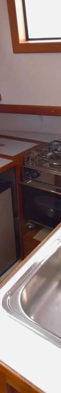 De foto toont een kombuis met een dubbele spoelbak, een fornuis met twee pitten, een koelkast en houten kasten.