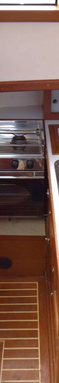 Een scheepskeuken met een tweepits gasfornuis met oven, twee roestvrijstalen spoelbakken en houten kasten.
