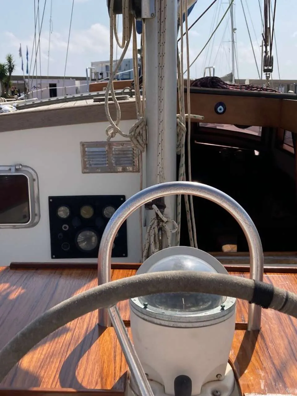 Een stuurwiel met kompas en een houten dashboard met diverse meters zijn zichtbaar in de kuip van een zeilboot.