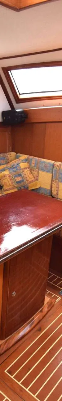De foto toont een houten interieur van een boot met een U-vormige bank en een losse bank, beide met geel-blauwe kussens…