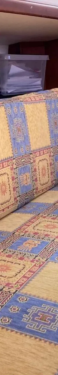 Een interieur van een boot met een bank met een kleurrijke, patroonrijke bekleding en houten kasten en panelen.