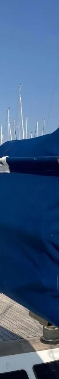 Een zeilboot met een blauwe zeilhoes en een houten dek ligt in een haven onder een helderblauwe lucht. — Endurance 44