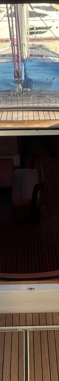 Een bovenaanzicht van het dek van een zeilboot met een open kajuitingang, omringd door touwen en lieren.