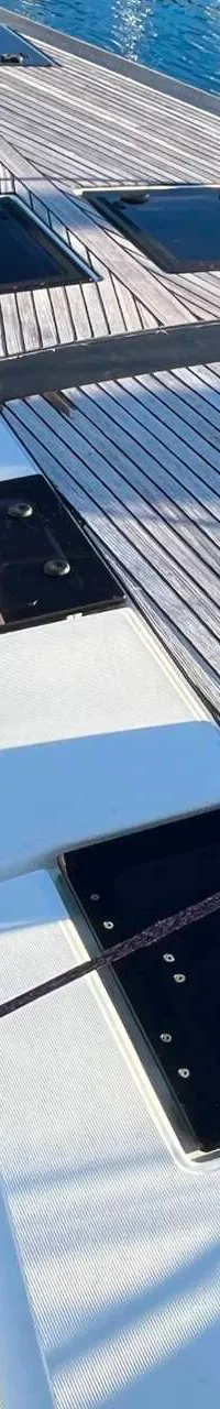 Een bovenaanzicht van het teakhouten dek van een zeilboot met luiken, lijnen en een mast. — Dufour 520 Grand Large