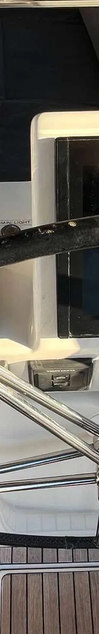 Een stuurwiel met een Raymarine-scherm en diverse bedieningselementen op een boot met teakhouten dek.