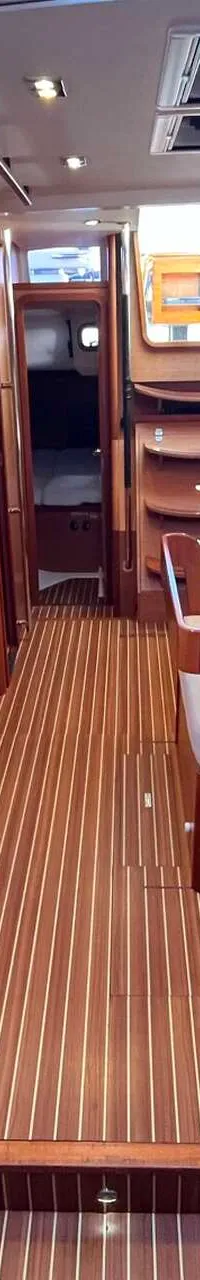 De foto toont het interieur van een boot met houten vloer en wanden, witte banken en een houten tafel.