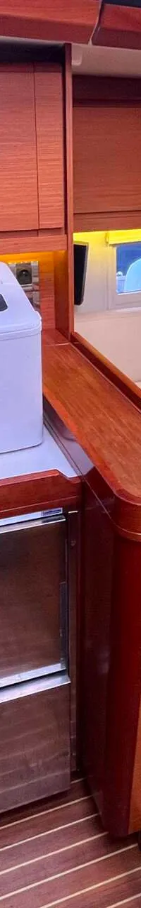 Een interieur van een boot met houten lambrisering, een wit aanrechtblad, een ijsmachine, twee koellades en een bank.