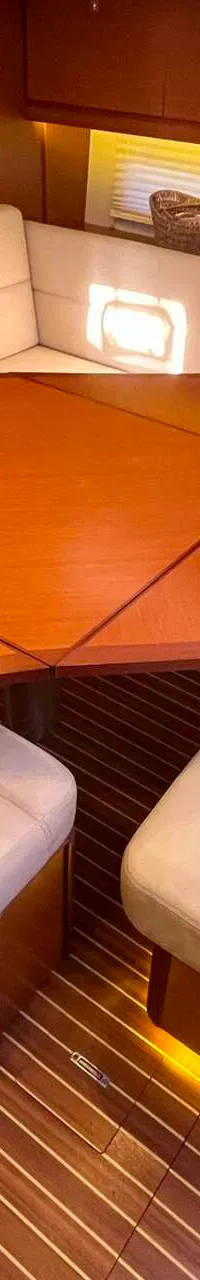 Een interieur van een boot met een houten tafel, crèmekleurige banken en stoelen, en een houten vloer met lichte strepen.